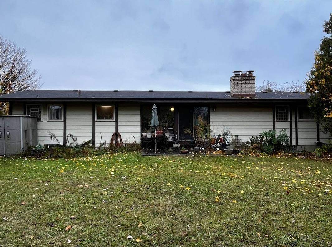 The same back of the house with the overgrowth gone: clean siding, every window and the chimney showing, and a green lawn.